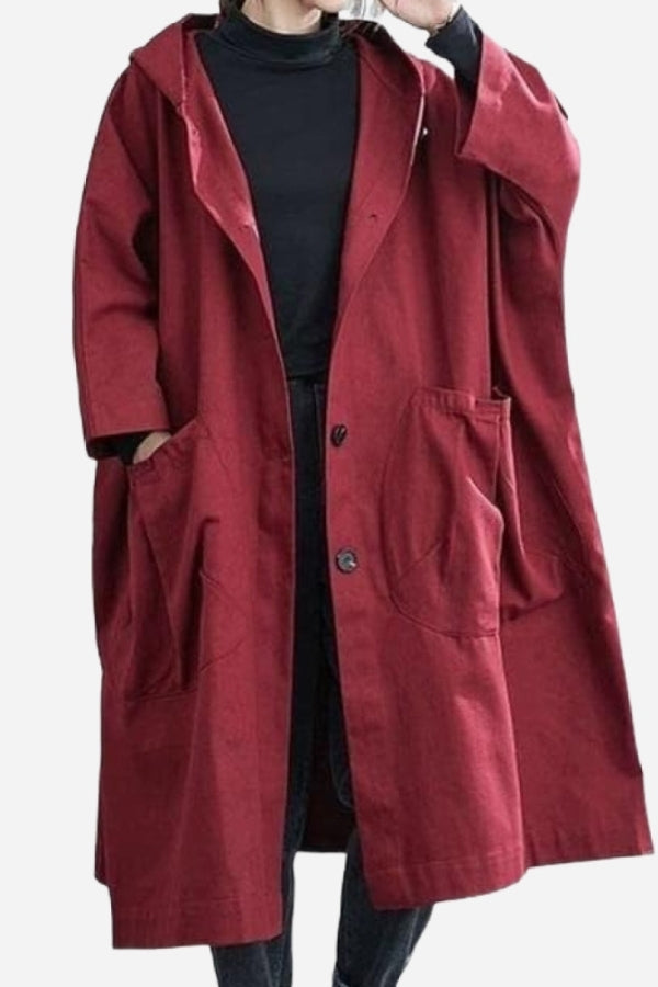 A person is shown wearing the looselyboho Burgundy One Size Fits All Oversized Waterproof Windbreaker Jacket over a black turtleneck. The long, loose-fitting, hooded maroon coat features large front pockets and an unbuttoned top for easy movement. Their hands rest comfortably in the jacket's pockets, offering both style and wind protection.