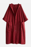 The Burgundy One Size Fits All Oversized Waterproof Windbreaker Jacket by looselyboho is a long, red raincoat with a hood. This robustly designed all-weather jacket features a button-up front and two large side pockets. The sleeves are rolled up to about elbow length, providing excellent wind protection.