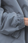 The image depicts a close-up of a person wearing The Windbreaker Jacket's POWDER BLUE WINDBREAKER. The focus is on the sleeve, which features an elastic cuff. With their arm slightly bent and part of their hand visible, the jacket exhibits a matte finish.