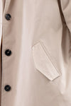 Close-up of a beige trench coat showing the side pocket and four black buttons. The fabric appears smooth and slightly shiny, suggesting it's a stylish BISCUIT BEIGE WINDBREAKER crafted from lightweight water-resistant material by looselyboho.